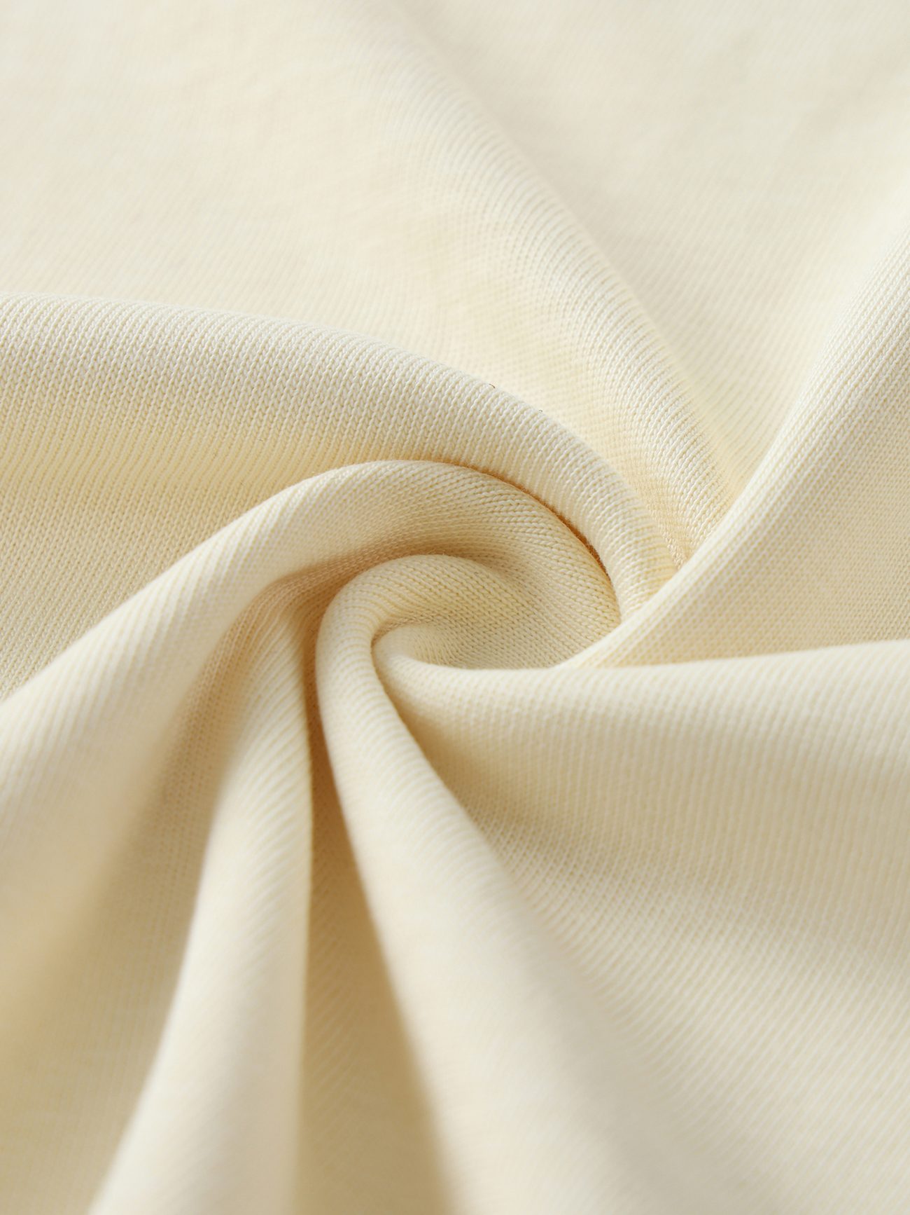 A close-up of the Crane Oversized Contrast-Stitched Cotton Tee shows cream cotton fabric with a smooth, soft texture in a twisted fold, highlighting its weave and gentle drape—ideal for affordable luxury clothing.